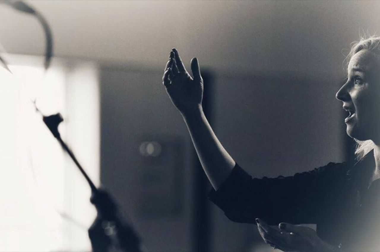 Profile of blonde-haired woman singing with her right arm raised