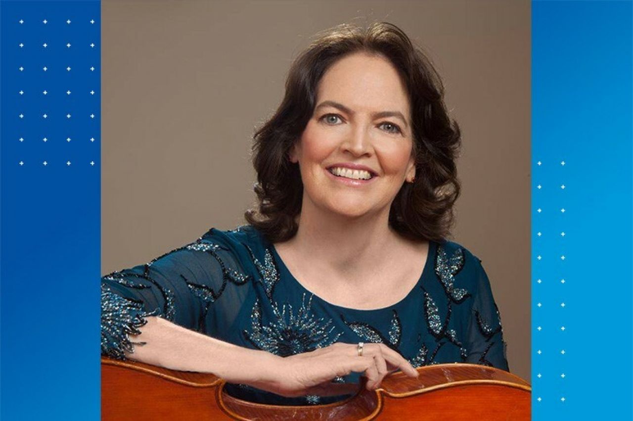 Head shot of a middle-aged woman with brown hair and a green shirt holding a cello