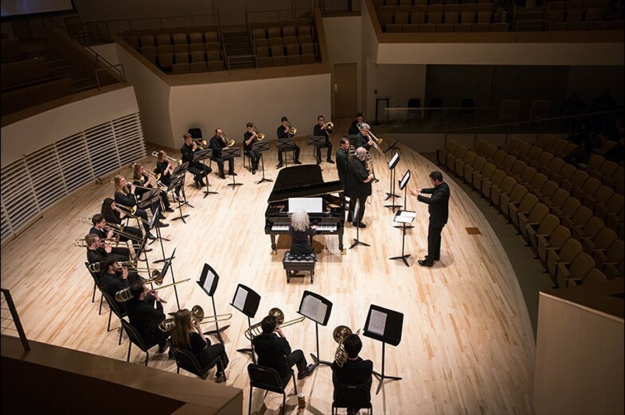Dimly lit stage with trombonists seated in a "U" shape with a piano in the middle
