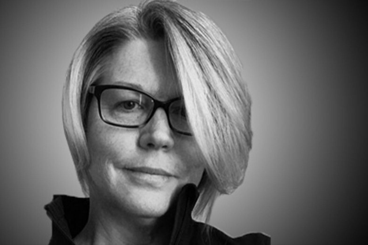 Black and white head shot of a woman with grey short hair and black-rimmed glasses