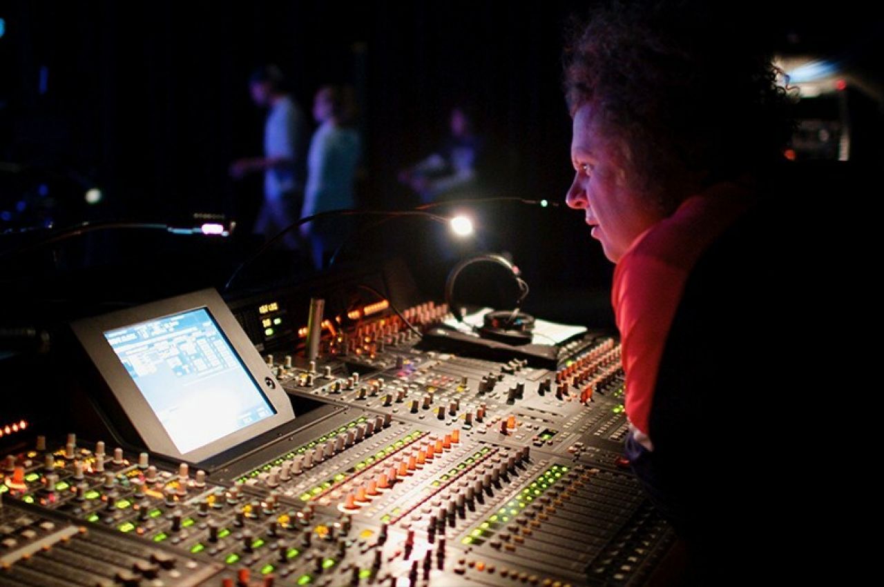 Man in red shirt leaning over a soundboard during a live performance