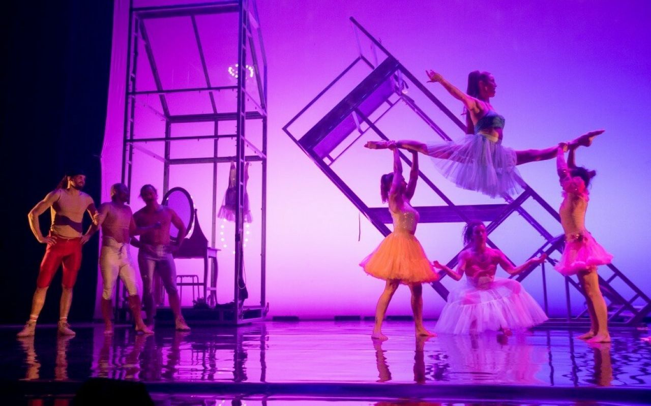 Three masculine-looking people watch in awe as a group of feminine-looking individuals perform feats of strength.