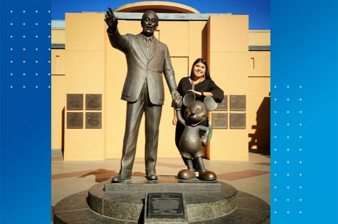 Woman with black hair smiling and standing next to a statue of Walt Disney holding Mickey Mouse's hand