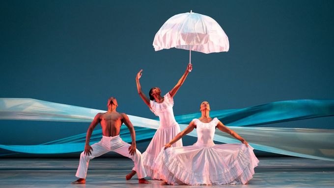 Three Black dancers stand in rigid, muscular poses as they all look upward.