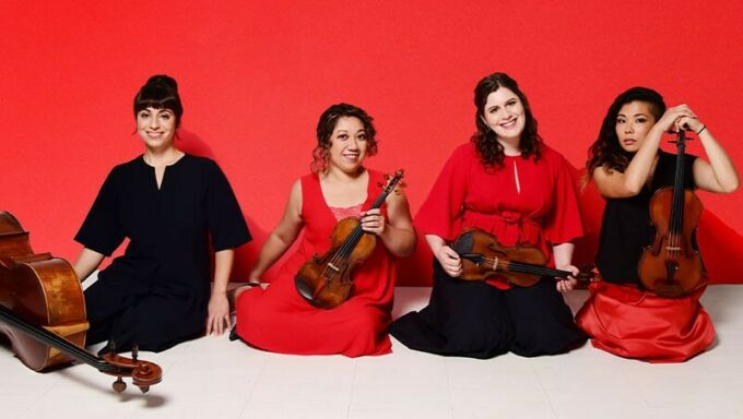 Four women sit in a row with their stringed instruments.