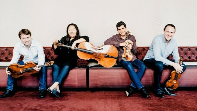 Four musicians sit on a couch and hold their classical instruments.