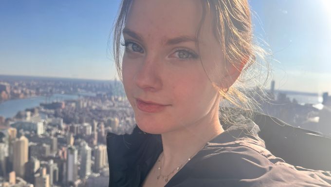 A selfie of Johnna D’Ecclesiis with a high-rise view of a city behind her.