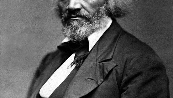 A man of color with a full head of hair and beard looks solemnly off the frame into the distance.