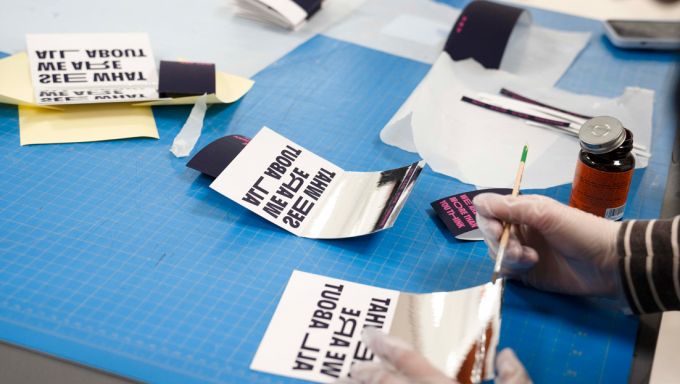 A blue drafting table with invitations atop that are being put together by hand.