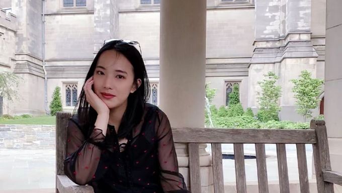 Young Asian woman with dark hair sitting on a bench and smiling