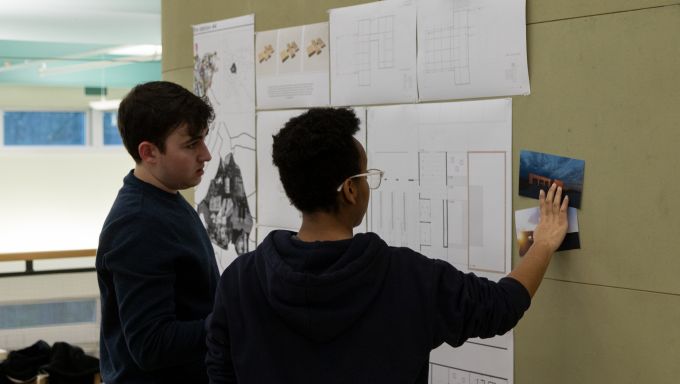 Two students looking at designs tacked to a wall