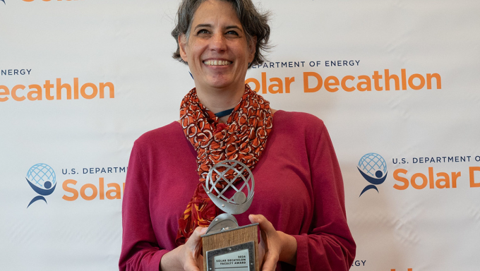 Lisa Iula holds a trophy in front of a U.S. Department of Energy Solar Decathlon background.