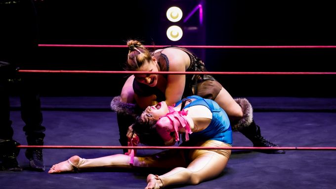 One wrestler bends backward at the waist while another wrestler pins on a wrestling mat.