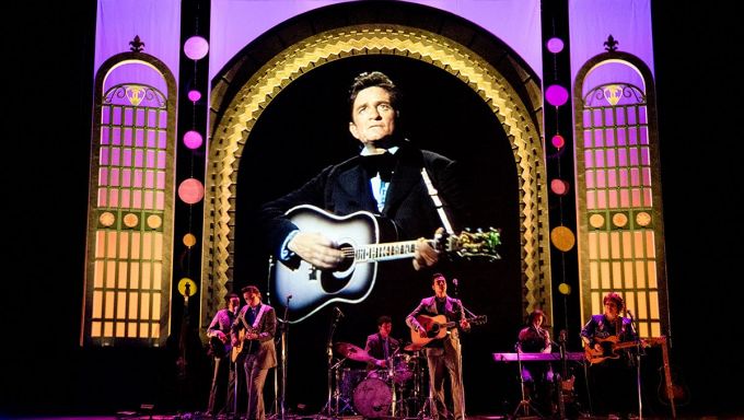 Johnny Cash is shown on a large videoscreen while a group of musicians perform live on the stage.