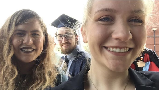Selfie of two young women and a young man wearing a graduation cap