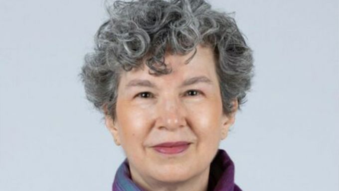 Head shot of a white woman with grey hair wearing a purple scarf and smiling