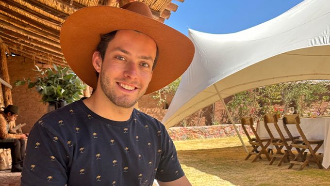 Young white man in blue shirt wearing a light brown hat while smiling