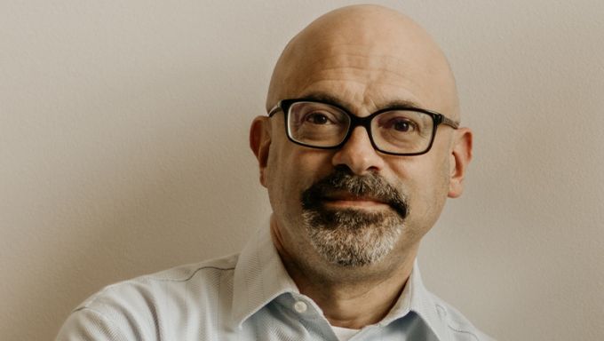 Head shot of a white man with a bald head wearing black-framed glasses