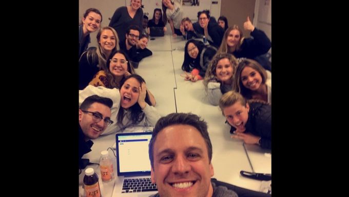 Ryan Russell takes a selfie with his students who surround a long table.