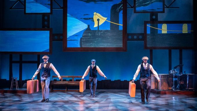 Three Black dancers each carry a suitcase as they step in unison.