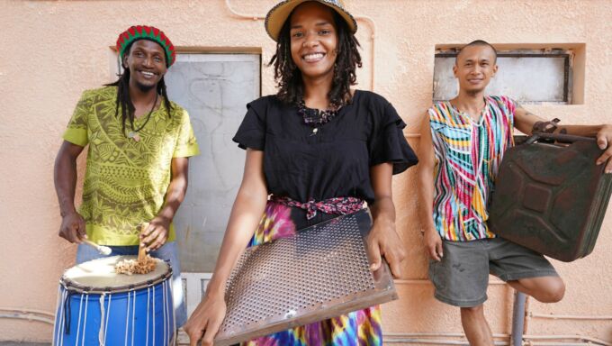 Three musicians hold their instruments made from beach trash.