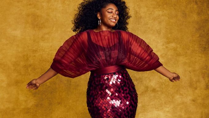 A young Black woman wears a designer sequined dress and lets the wind blow through her hair during a photo shoot.