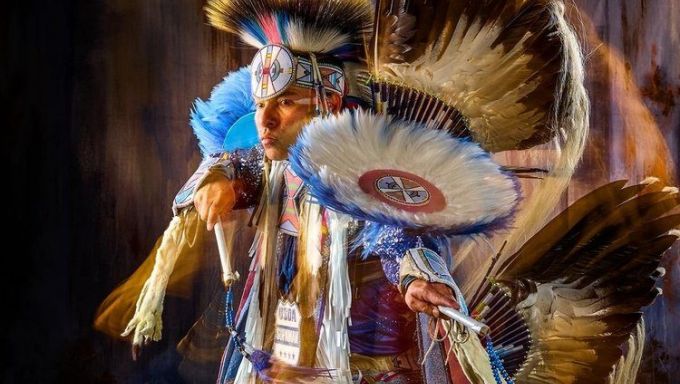 A Native American man dressed in full tribe regalia looks off into the distance.