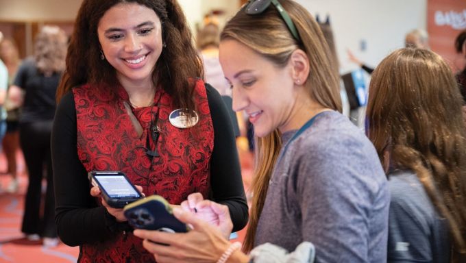 A young woman assists another woman with accessing tickets on her mobile phone.