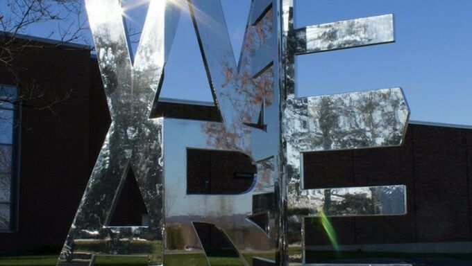 A mirrored statue in the shape of the words We Are reflects its surroundings.