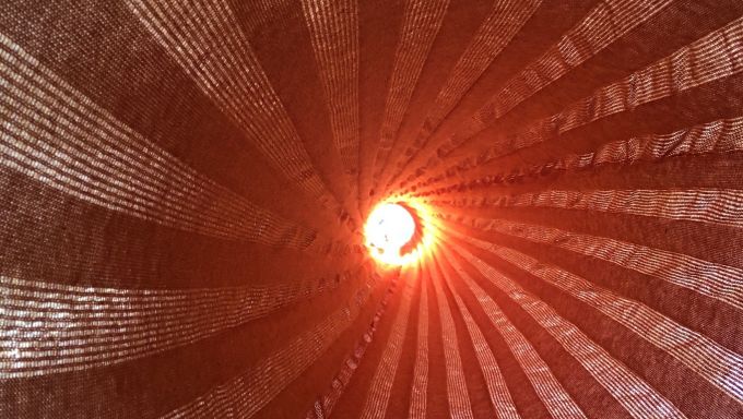 Abstract image of woven fabric in a spiral pattern with a red light shinning through the center