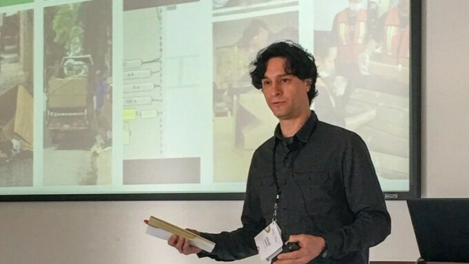 Julio Diarte stands to the right, motioning to a screen behind him which is displaying his research during a presentation.