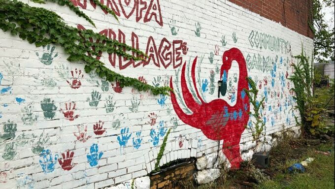 A brick wall that is painted white with a flamingo painted on it as well as Sankofa Village and the handprints of children in blue and red.