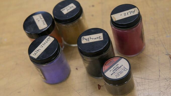 Six small glass bottles with black lids labeled with the names of colors and filled with various paint colors