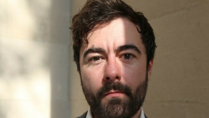 Headshot of a man with short, wavy brown hair and matching beard