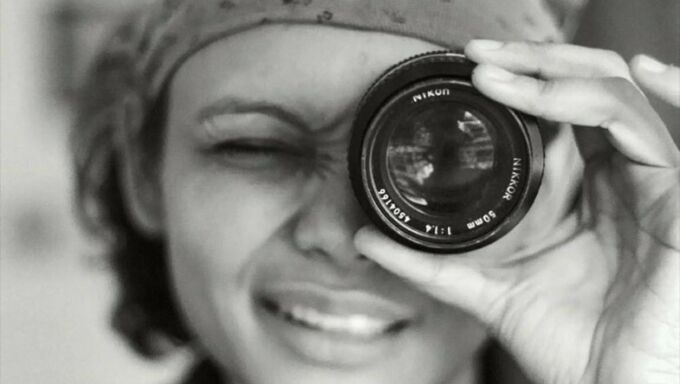 Black and white photo of a woman with short dark hair looking through a camera lens