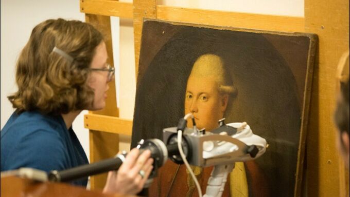 Profile shot of an art historian examining a portrait with an electronic scanning device.