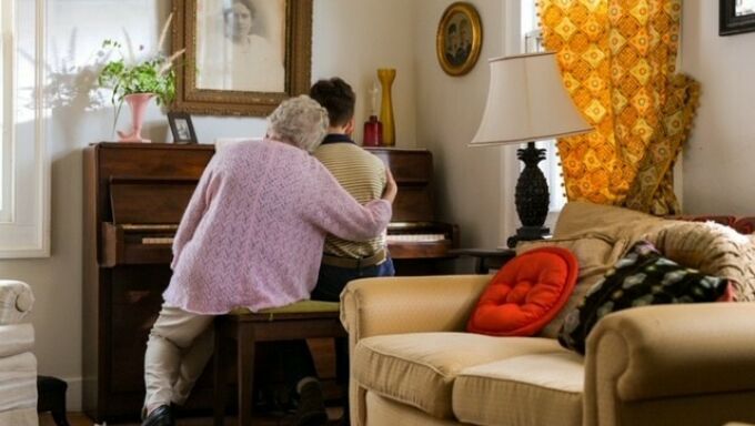 An elderly woman sitting on a piano bench hugging man next to her