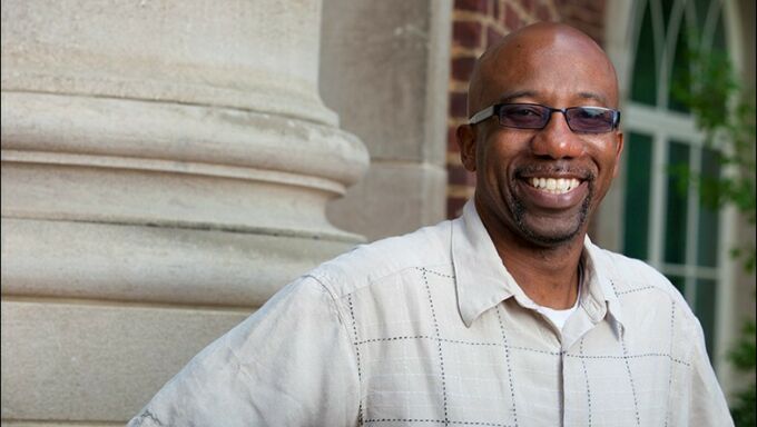 Bald Black man with dark glasses and a goatee smiling