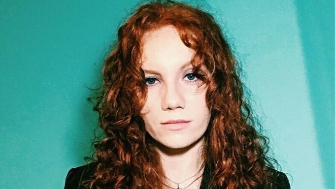 Headshot of a young woman with red hair in front of a teal green background