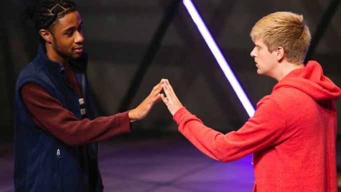 A Black young man and a white young man stand face to face touching hands