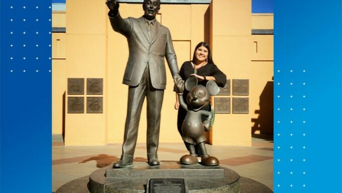 Woman with black hair smiling and standing next to a statue of Walt Disney holding Mickey Mouse's hand