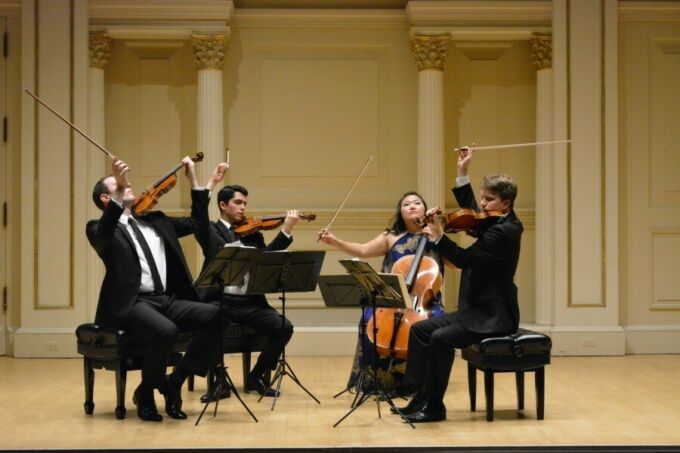 Three men and a woman sit on stage and perform on classical instruments.