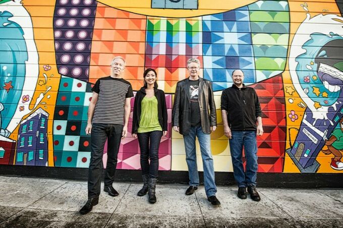 Three men and a woman stand against a wall painted over with a mural.