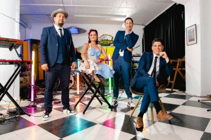 Four artists fear dapper formal clothing and pose in a boldly decorated room for a camera.