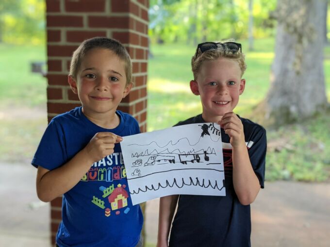 Two young boys smile while holding up a drawing between them.