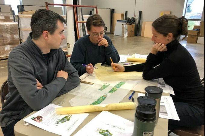 Julian Revie, Becca Newburg and Gillean Denny surround a table with design plans laid before them.