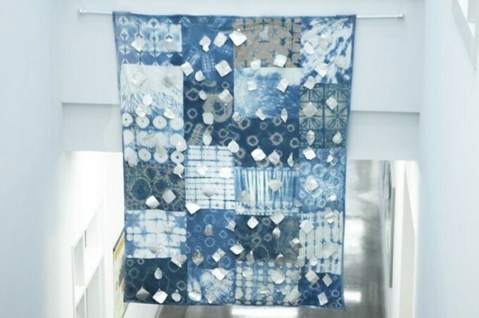 Indigo-colored quilt that is about 10 feet tall and six feet wide hanging in the entryway of a well-lit building
