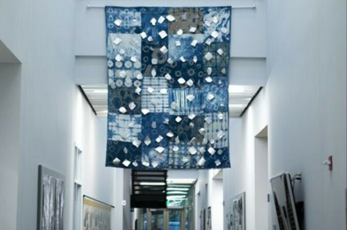 An indigo-colored quilt with medallions affixed on the front of the piece hangs in a well-lit hallway