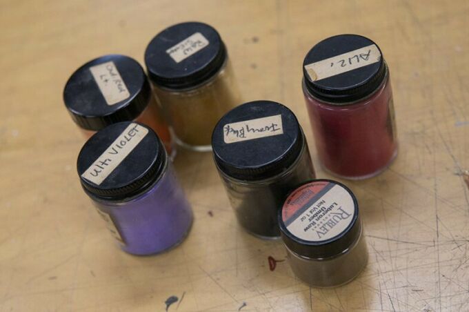 Six small glass bottles with black lids labeled with the names of colors and filled with various paint colors