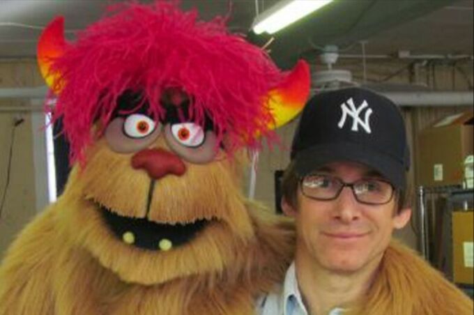 Man with New York Yankees blue hat holding a puppet with red hair and horns
